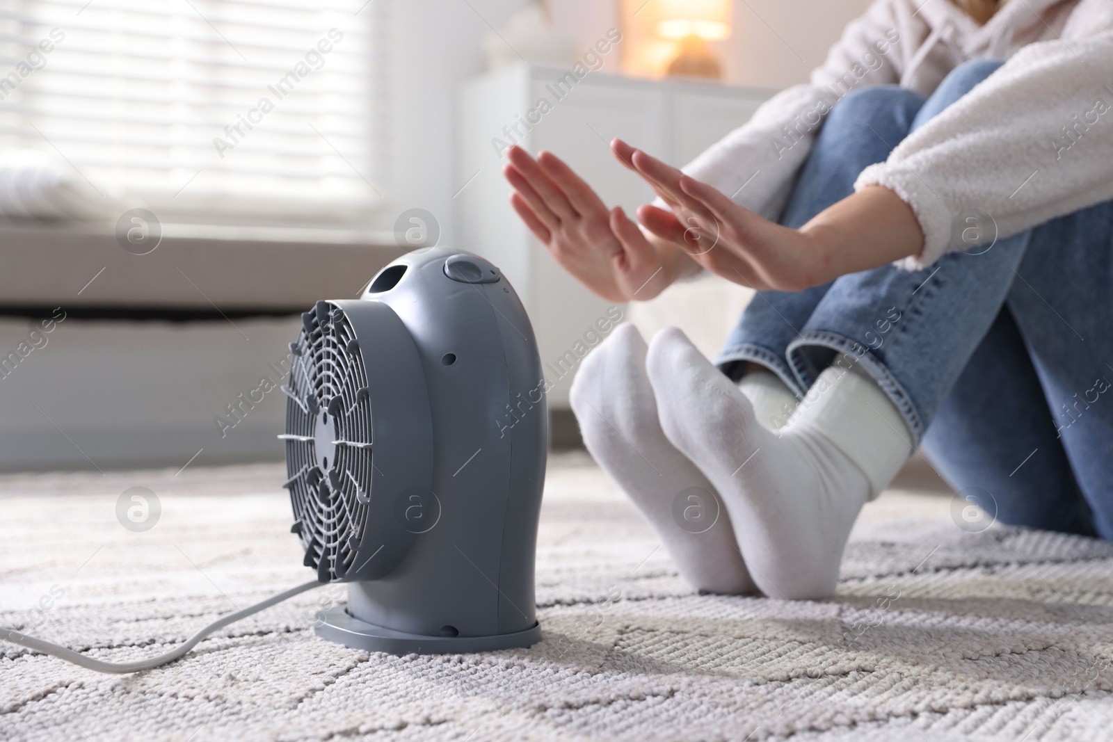Photo of Young woman near electric heater on floor at home, closeup