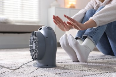 Photo of Young woman near electric heater on floor at home, closeup
