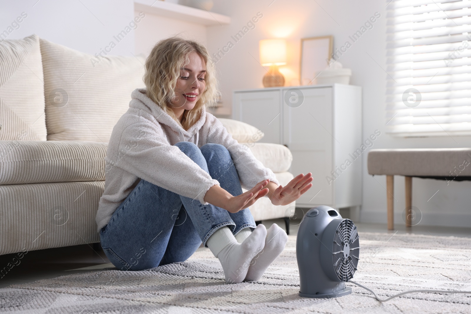 Photo of Young woman near electric heater on floor at home