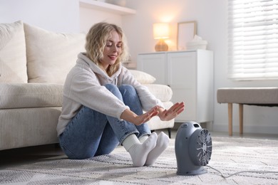 Photo of Young woman near electric heater on floor at home