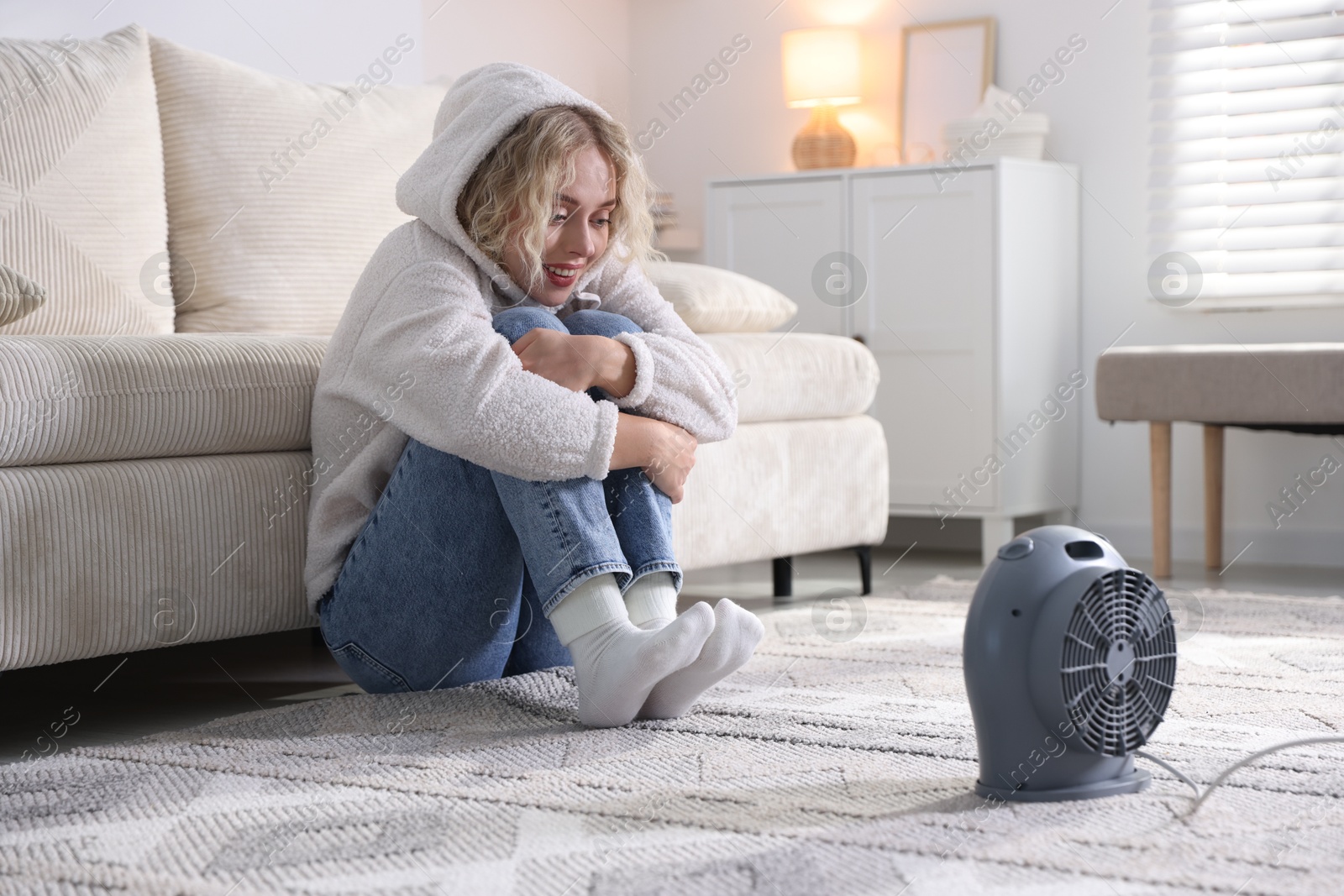 Photo of Young woman near electric heater on floor at home