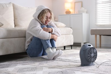 Photo of Young woman near electric heater on floor at home