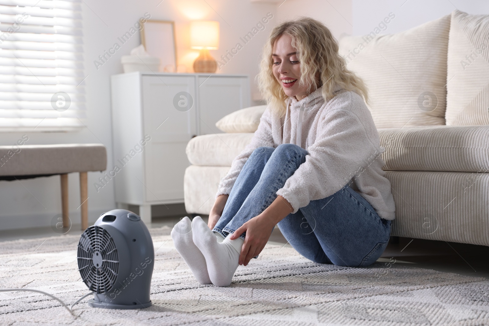 Photo of Young woman near electric heater on floor at home