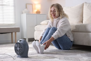 Photo of Young woman near electric heater on floor at home
