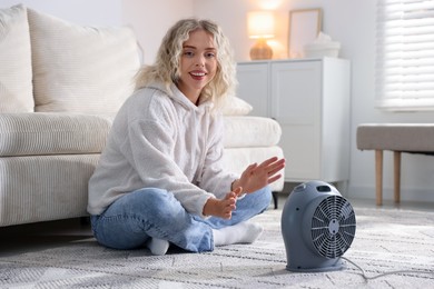 Photo of Young woman near electric heater on floor at home