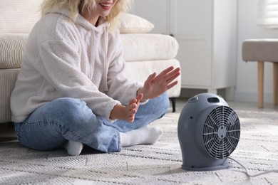 Photo of Young woman near electric heater on floor at home, closeup