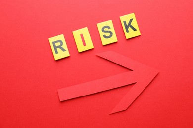Photo of Word Risk and arrow on red background, flat lay