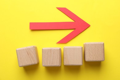 Photo of Red arrow and blank wooden cubes on yellow background, flat lay. Space for text