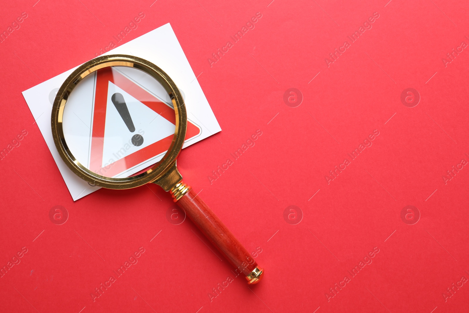Photo of Risk. Sheet of paper with warning sign and magnifying glass on red background, top view. Space for text