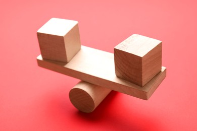 Photo of Risk. Wooden seesaw scale with cubes on red background, closeup