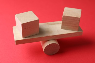 Photo of Risk. Wooden seesaw scale with cubes on red background, closeup
