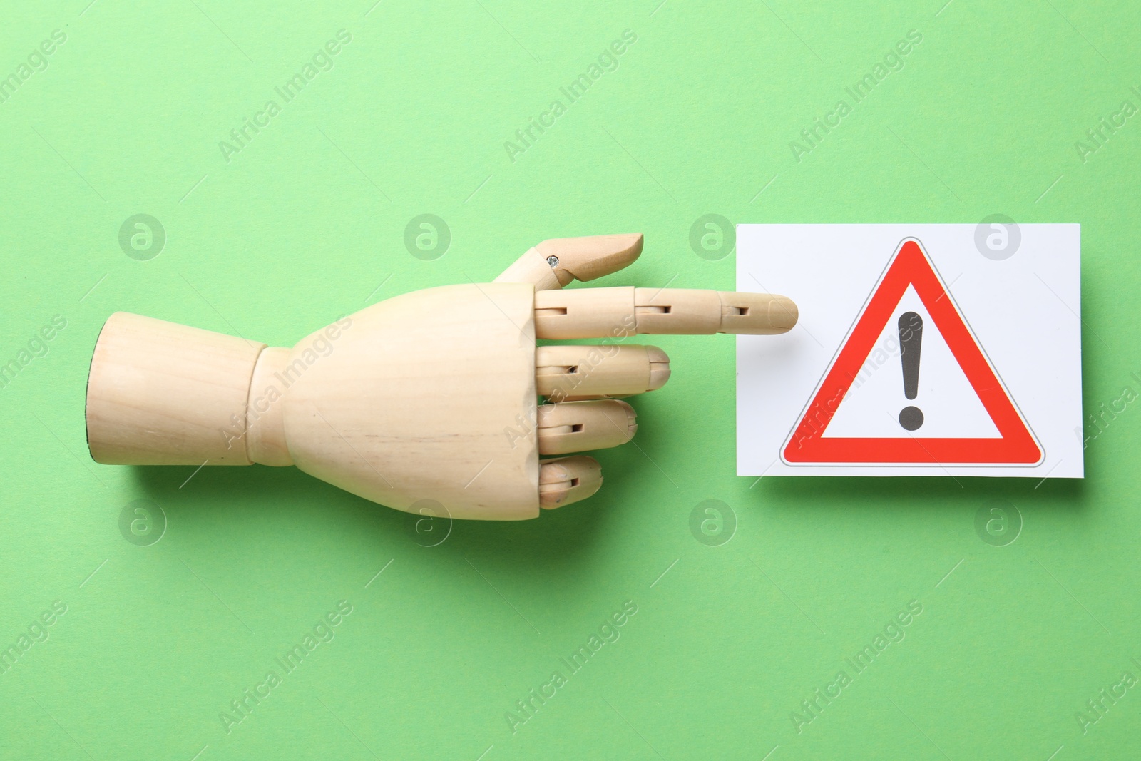 Photo of Risk. Mannequin hand pointing at sheet of paper with warning sign on green background, flat lay