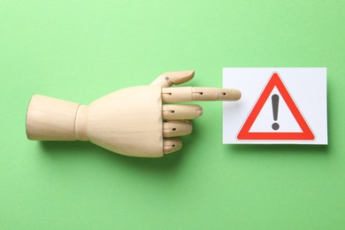 Photo of Risk. Mannequin hand pointing at sheet of paper with warning sign on green background, flat lay
