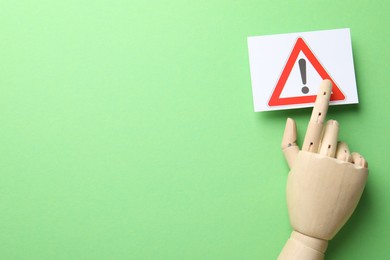 Photo of Risk. Mannequin hand pointing at sheet of paper with warning sign on green background, flat lay. Space for text