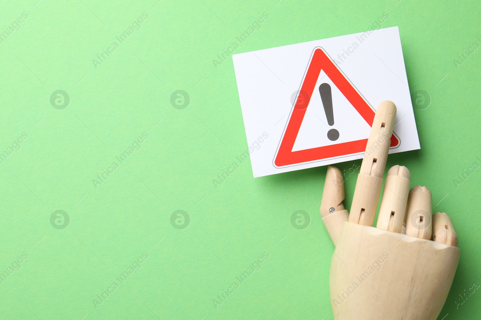 Photo of Risk. Mannequin hand pointing at sheet of paper with warning sign on green background, flat lay. Space for text