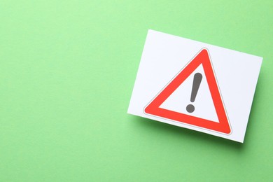 Photo of Risk. Sheet of paper with warning sign on green background, top view and space for text