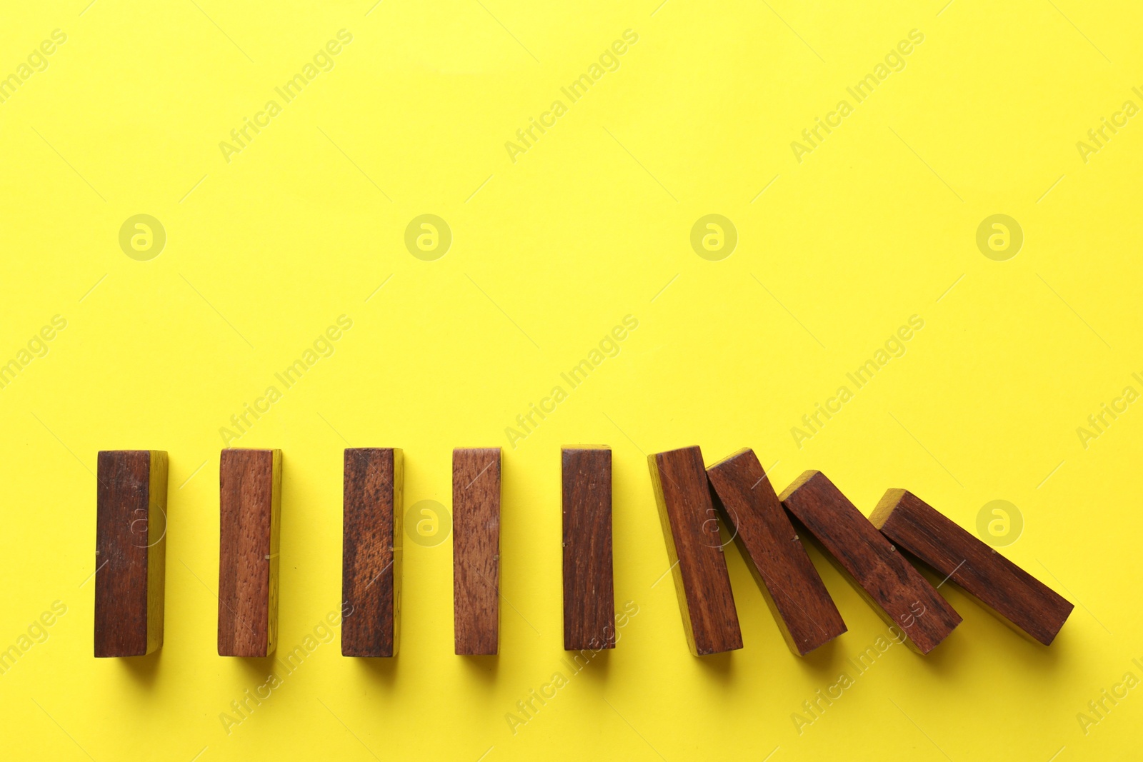 Photo of Risk. Wooden blocks falling on yellow background, flat lay with space for text