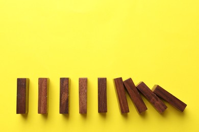 Photo of Risk. Wooden blocks falling on yellow background, flat lay with space for text