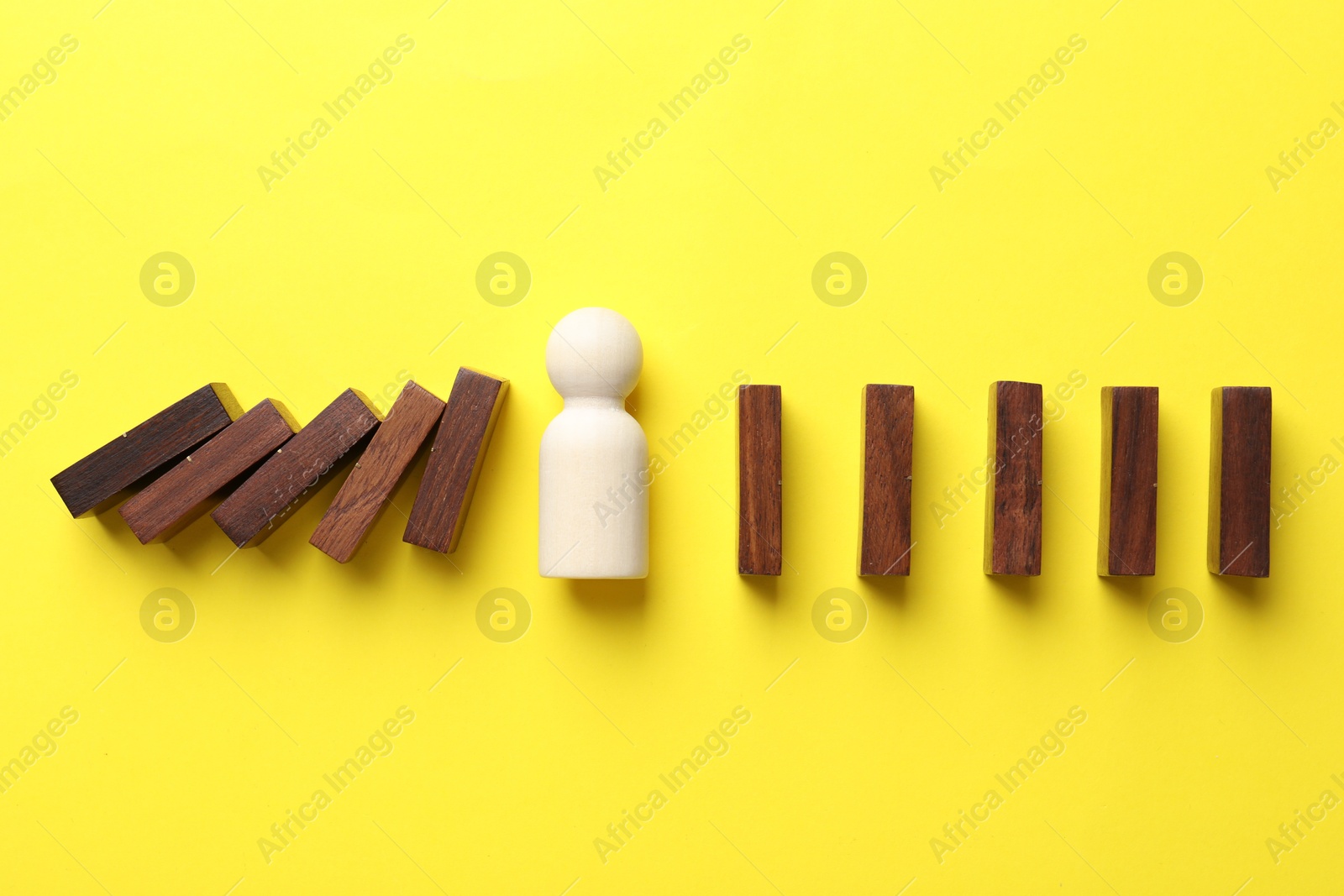 Photo of Risk. Wooden figure between falling blocks and laying ones on yellow background, flat lay