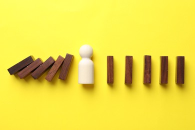 Photo of Risk. Wooden figure between falling blocks and laying ones on yellow background, flat lay