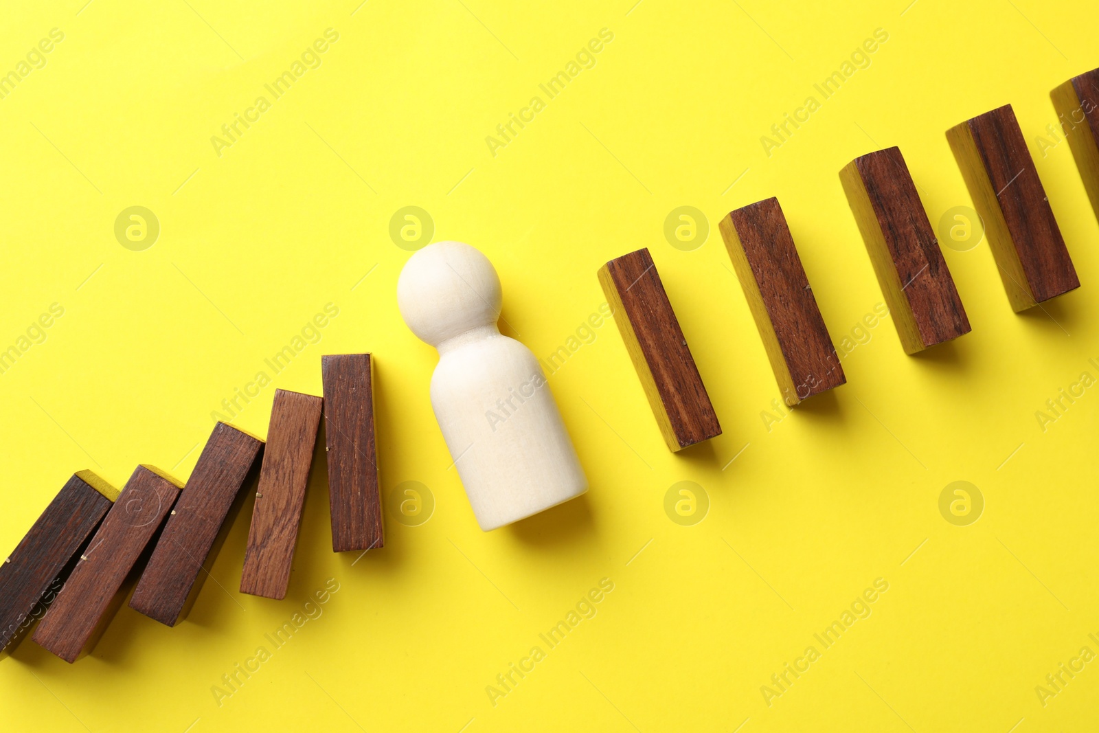 Photo of Risk. Wooden figure between falling blocks and laying ones on yellow background, flat lay