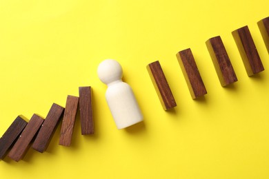 Photo of Risk. Wooden figure between falling blocks and laying ones on yellow background, flat lay