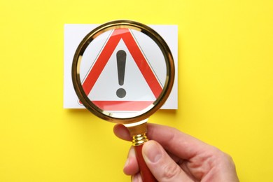 Photo of Risk. Woman with magnifying glass and warning sign on yellow background, top view