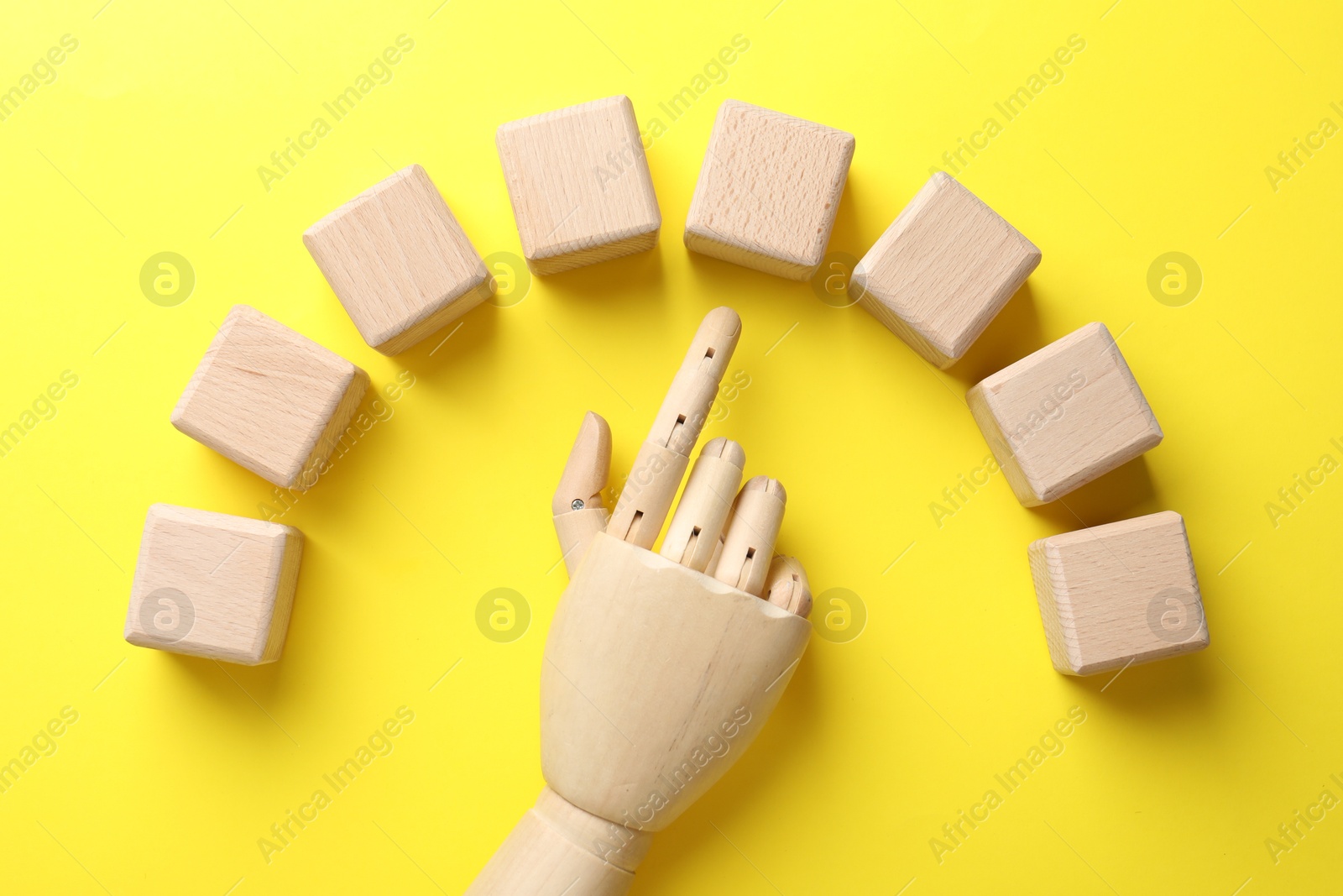 Photo of Mannequin hand pointing at blank wooden cubes on yellow background, flat lay with space for text