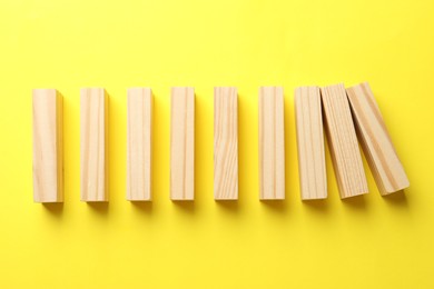 Photo of Risk. Wooden blocks falling on yellow background, flat lay with space for text