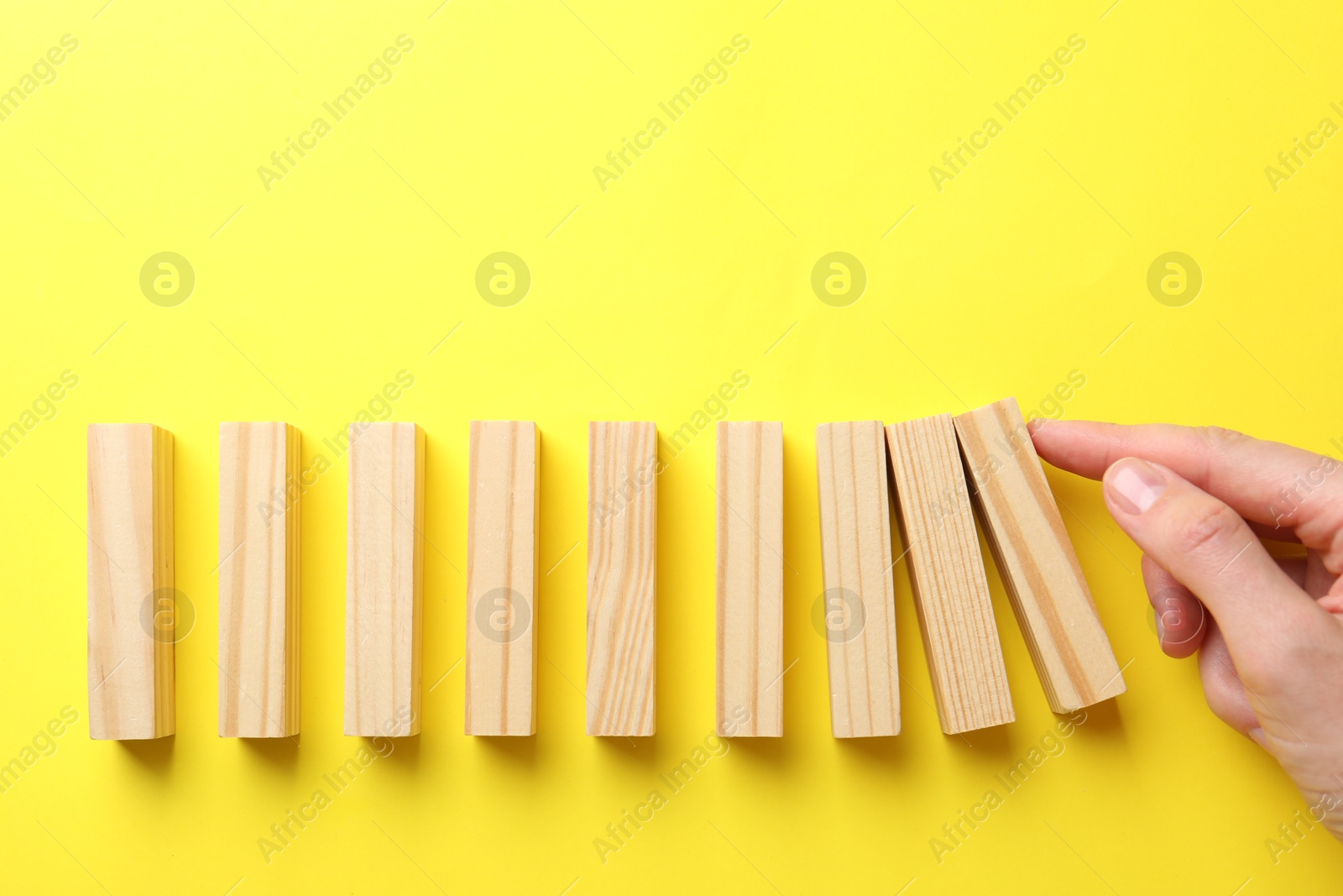 Risk. Woman pushing wooden blocks on yellow background, top view with space for text Photo of Risk. Woman pushing wooden blocks on yellow background, top view with space for text