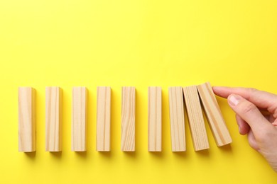 Photo of Risk. Woman pushing wooden blocks on yellow background, top view with space for text