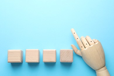 Photo of Blank cubes and mannequin hand on light blue background, flat lay. Space for text