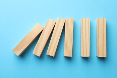 Photo of Risk. Wooden blocks falling on light blue background, flat lay with space for text