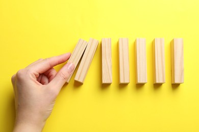 Photo of Risk. Woman pushing wooden blocks on yellow background, top view with space for text