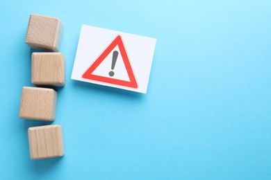 Photo of Blank cubes and sheet of paper with warning sign on light blue background, flat lay. Space for text
