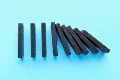 Photo of Risk. Black blocks falling on light blue background, flat lay
