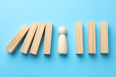 Photo of Risk. Wooden figure between falling blocks and laying ones on light blue background, flat lay