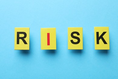 Photo of Risk concept. Yellow cards with letters on light blue background, flat lay