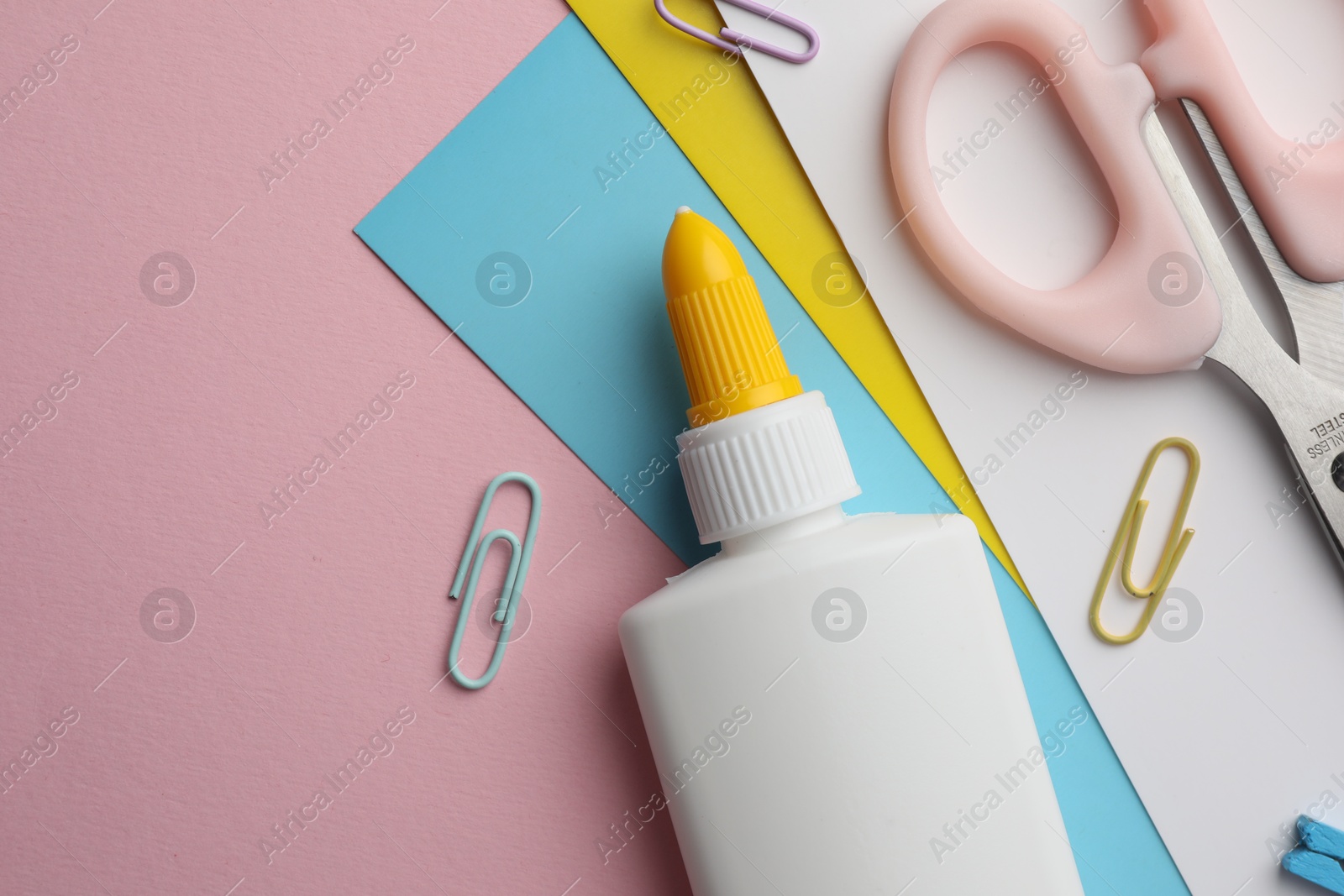Photo of Glue in bottle, color paper and other stationery on pink background, flat lay. Space for text