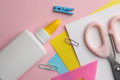 Photo of Glue in bottle, color paper and other stationery on pink background, flat lay