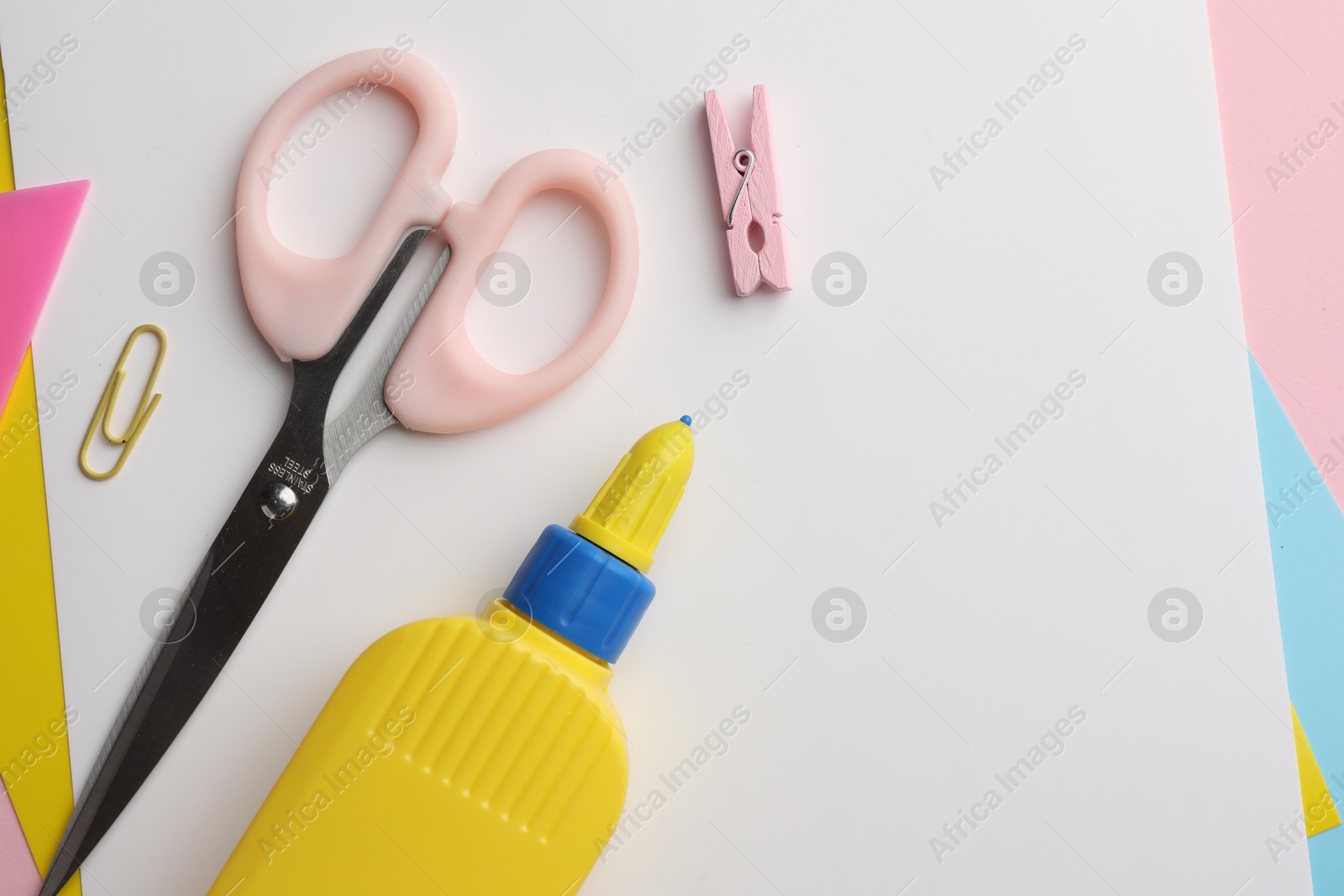 Photo of Glue in bottle, color paper and scissors on pink background, flat lay. Space for text