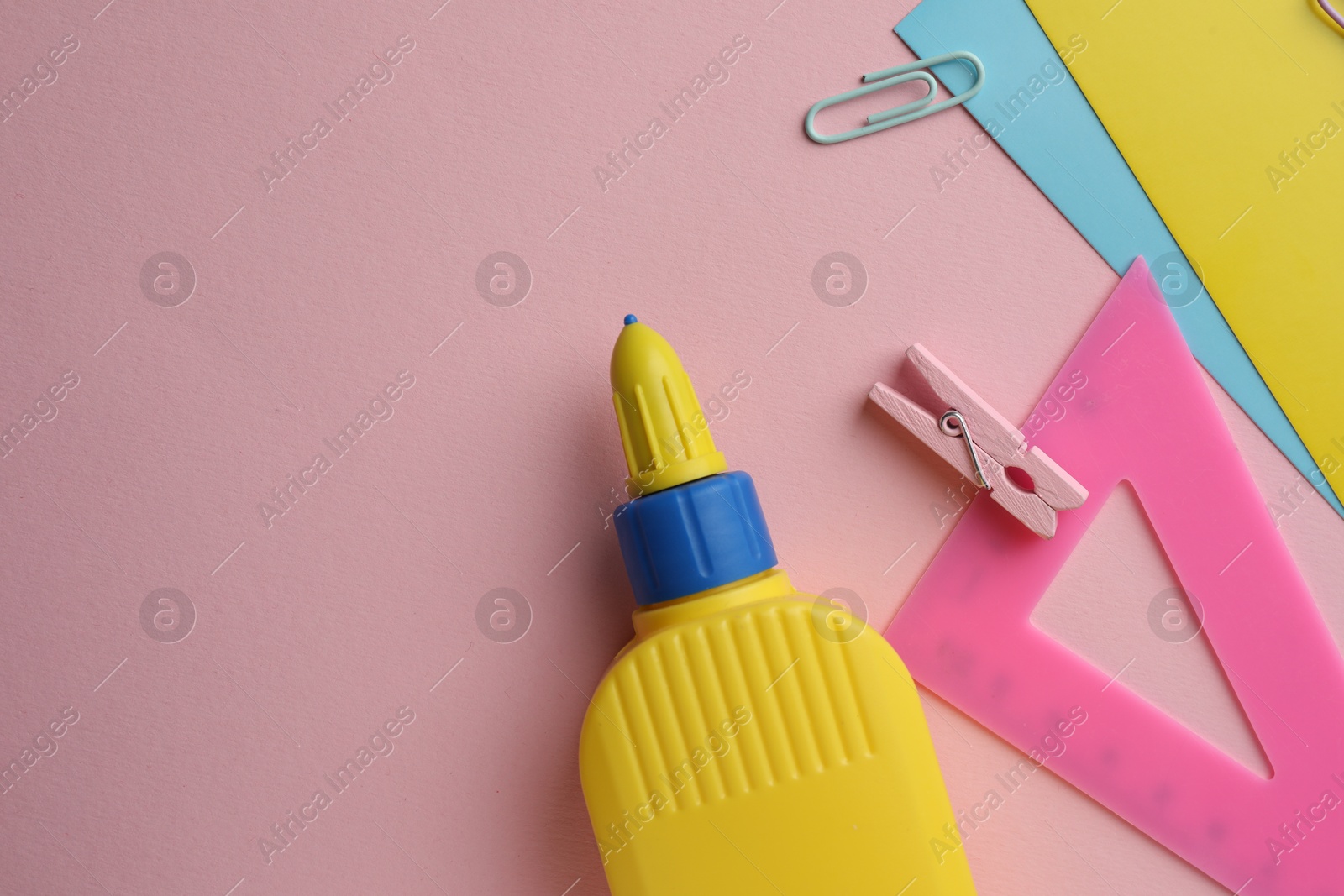 Photo of Glue in bottle, color paper and ruler on pink background, flat lay. Space for text