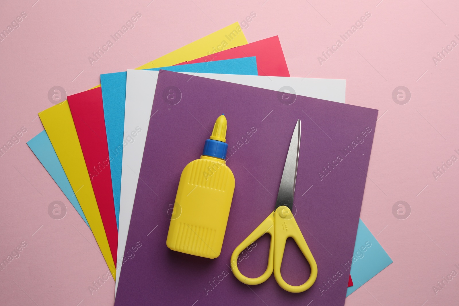 Photo of Glue in bottle, scissors and color paper on pink background, flat lay