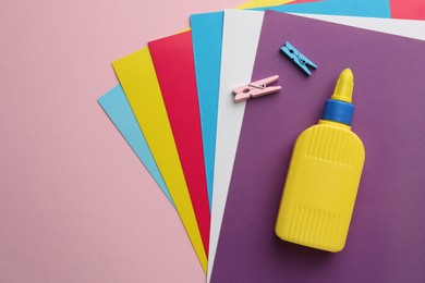 Photo of Glue in bottle and color paper on pink background, flat lay. Space for text
