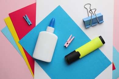 Photo of Glue in bottle, color paper and other stationery on pink background, flat lay