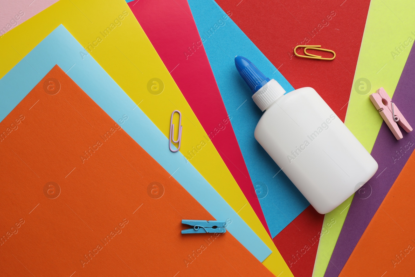 Photo of Glue in bottle and paper clips on color paper, flat lay. Space for text