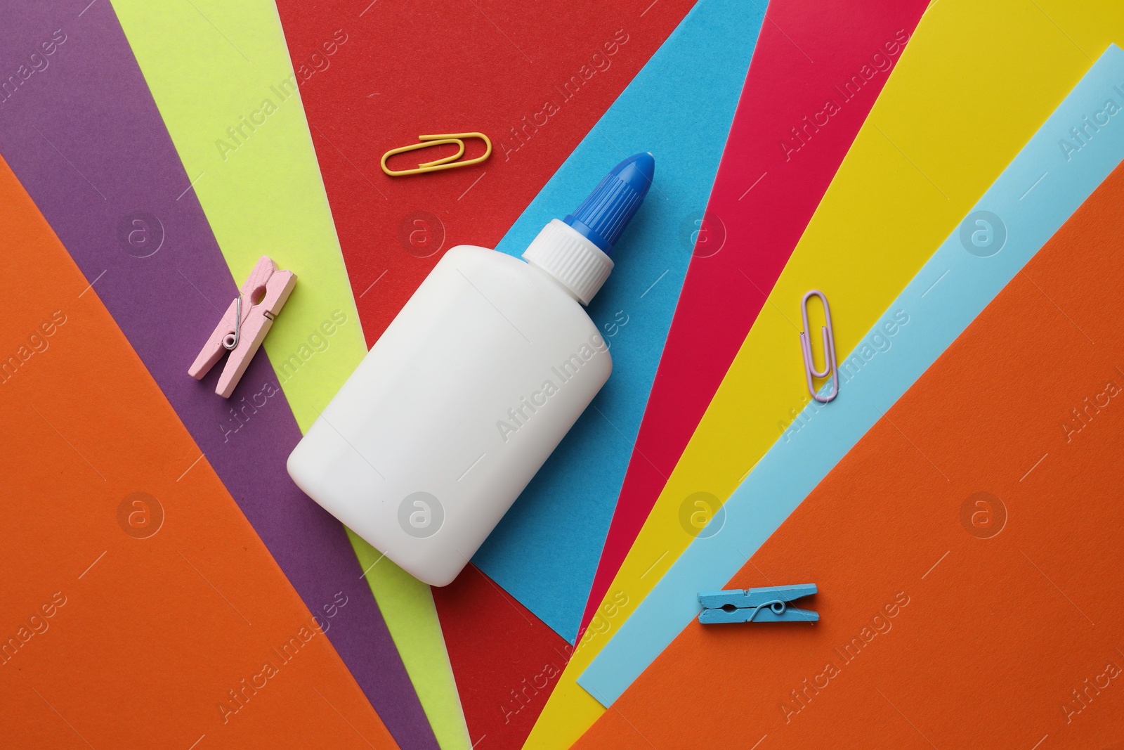 Photo of Glue in bottle and paper clips on color paper, flat lay