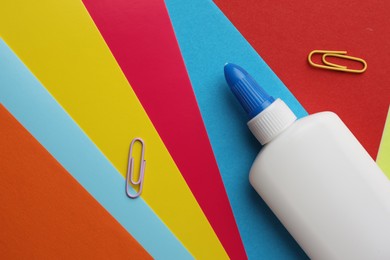 Photo of Glue in bottle and paper clips on color paper, flat lay. Space for text