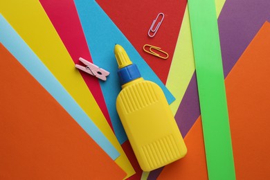 Photo of Glue in bottle and paper clips on color paper, flat lay