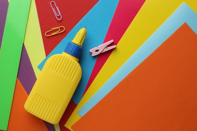 Photo of Glue in bottle and paper clips on color paper, flat lay. Space for text